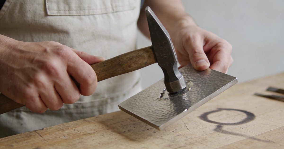 Artisan tenant un marteau repoussant une plaque metal