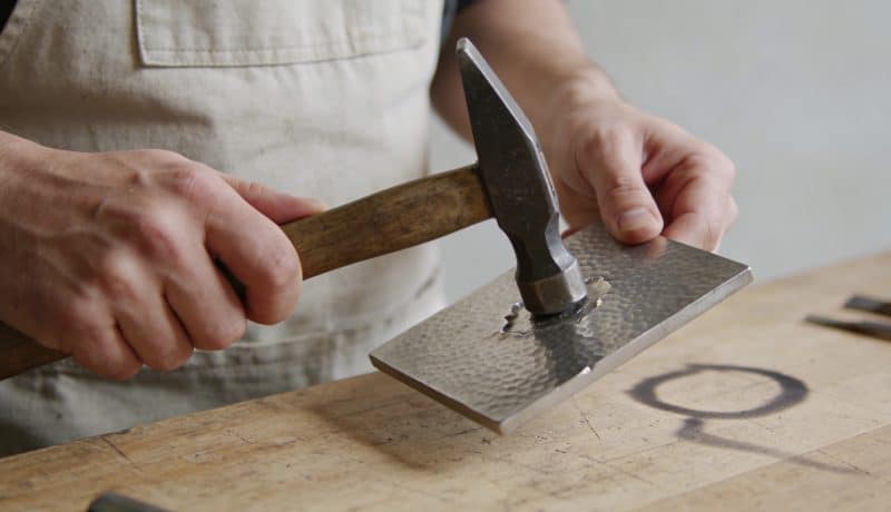 Artisan tenant un marteau repoussant une plaque metal