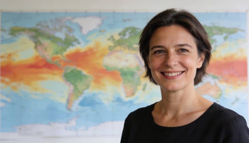Evelyne Dheliat souriante devant cartes meteo colorées
