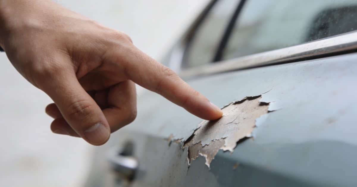 gros plan main pointant peinture voiture ecaillée