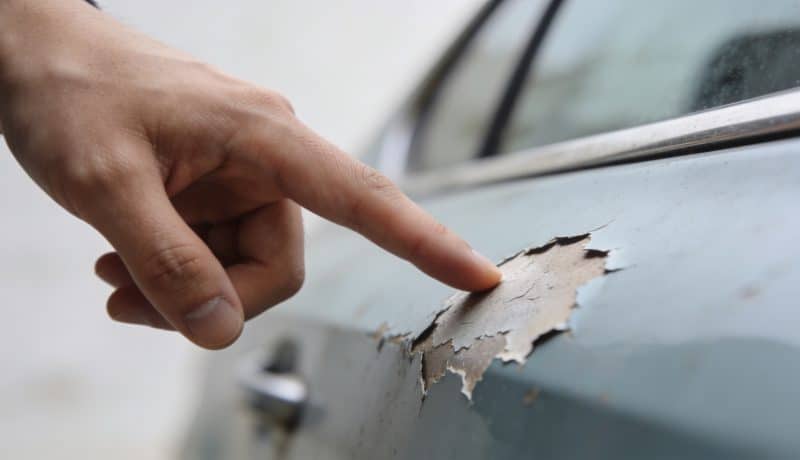 gros plan main pointant peinture voiture ecaillée