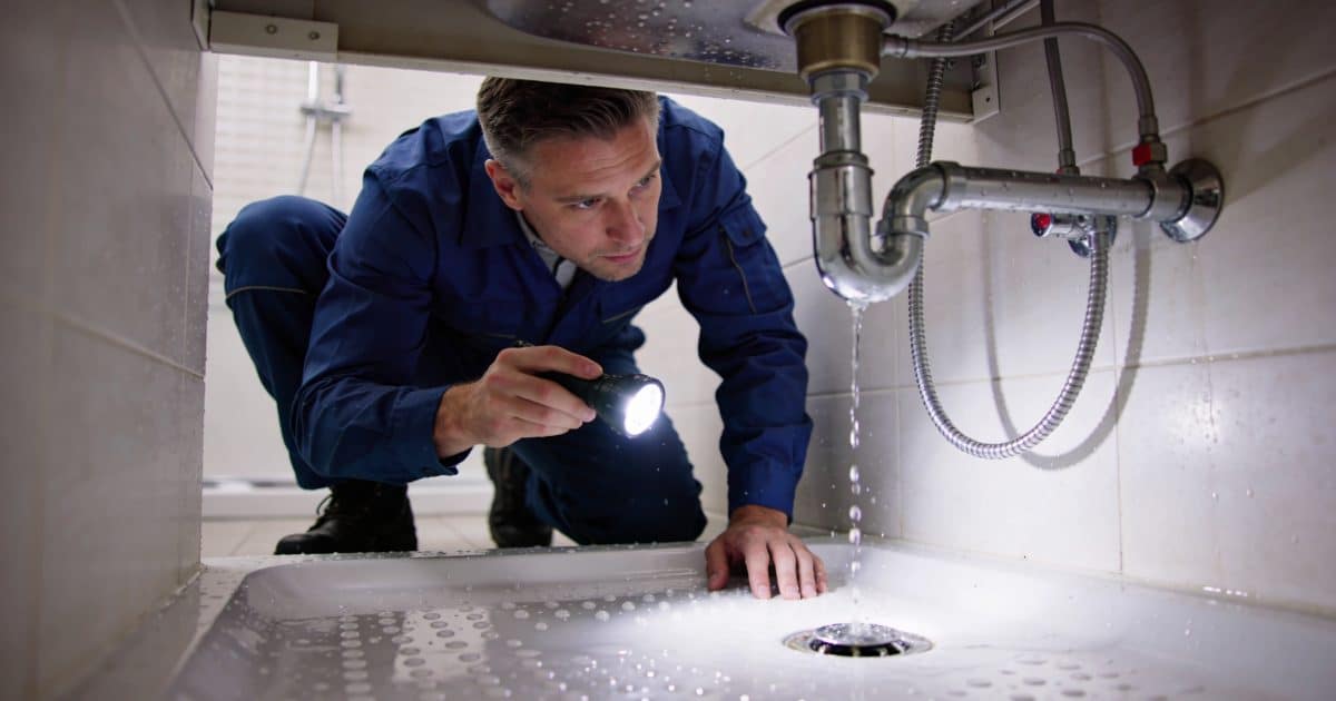 plombier accroupi inspectant une fuite sous douche