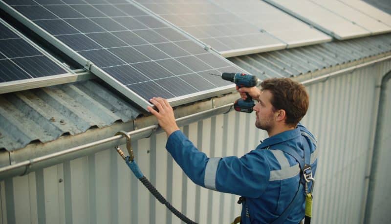 technicien installe panneaux solaires sur toit industriel